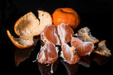 Fresh organic tangerines, whole and sliced, with reflection on shiny black background