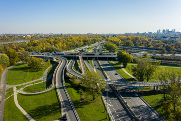 Drone shot at a highway with a clover junction with bridges and ramps, heavy traffic. Warsaw, Poland. Aerial view at the intersection of a large road in Warsaw, with traffic.