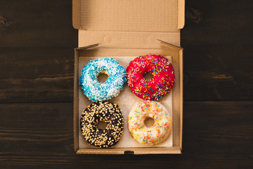 Delicious donuts lying on carton box on wooden background. Concept of donuts delivery.