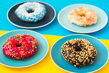 Fototapeta na wymiar Fresh appetizing 4 donuts lying on plate in colored yellow and blue background. Concept of sweet food.