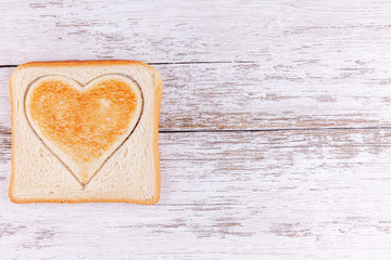 Toasted bread with cutted heart on white wooden table background. Concept morning meal with love and Happy Valentine's Day. Copy space.