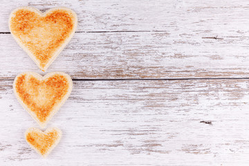 Group of toasted bread hearts together in a row on white wooden table background with copy space. Concept of breakfast in happy family.