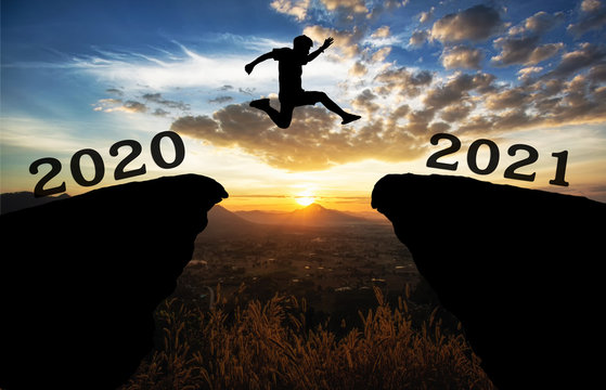 A young man jump between 2020 and 2021 years over the sun and through on the gap of hill  silhouette evening colorful sky. happy new year 2021.