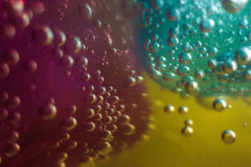 Macrophotography of air bubbles on the wall and bottom of a glass and pieces of ice in a soda drink. Gas bubbles are visible through the liquid, multi-colored illumination at the bottom of the glass