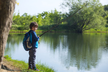 A boy with a backpack stands on the lake with a wooden stick.