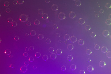 Macrophotography of air bubbles on the wall and bottom of a glass and pieces of ice in a soda drink. Gas bubbles are visible through the liquid, multi-colored illumination at the bottom of the glass