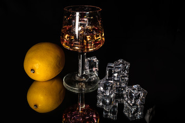 Alcohol drink in a glass whole lemon and ice cubes with reflection on shiny black background