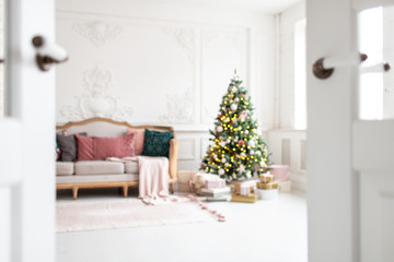Blurred photo of white sofa standing next to christmas tree surrounded by gift boxes