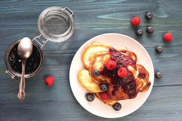  Homemade pancakes with fresh jam and berries - blueberries, strawberries on blue rustic table. Top view, flat lay, selective focus. Country organic style breakfast.     