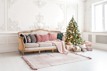 Christmas tree surrounded by giftboxes stands close to sofa in living room