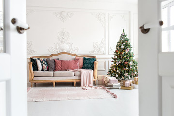 White sofa standing next to christmas tree surrounded by gift boxes. Selective focus