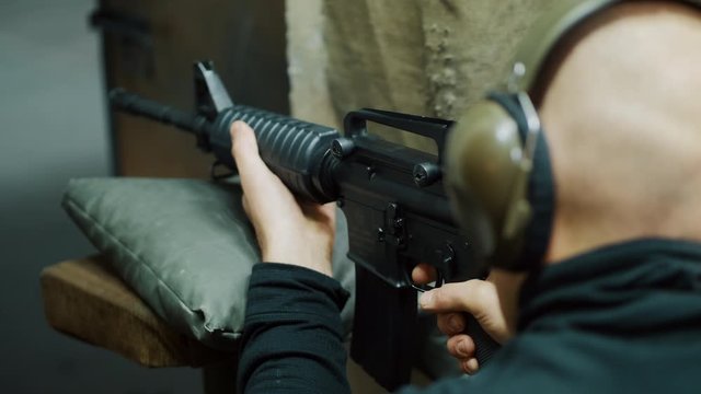 A man shoots with an automatic carbine at a shooting gallery, he is wearing headphones, takes aim at a target, firing training in the shooting gallery. Close-up 4k slow-motion video