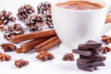 Cup of hot chocolate with cinnamon, anise stars, pieces of dark chocolate and some cones	