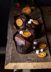 Three Tasty Homemade Chocolate Muffins in Paper Decorated with Marshmallow and Dried Citrus Vertical Wooden Background