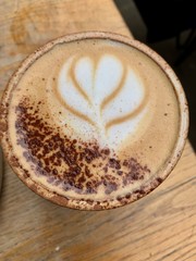 Cup of Cappuccino in a white cup sitting on a wooden table with flower latte art on the top
