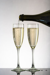 Two glasses with white wine and champagne next to the bottle on a colored background