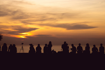 Fototapeta na wymiar silhouette group of people sitting look at sunset light with orange sky at Phuket, Thailand