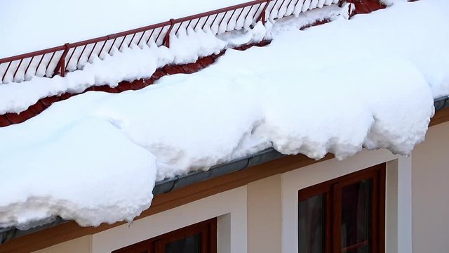 The Melting snow hang out from the roof. Dangerous snow falls on streets of the house on the street in the winter city.