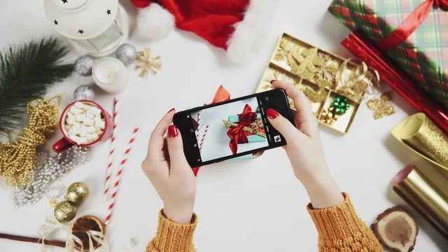 Woman taking beautiful picture on the smart phone. Female hands photogtaphing Christmas present on white table.