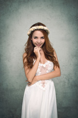 Vintage style portrait beautiful woman wearing a white dress, flower crown on gray soft blurred background.