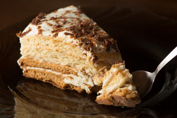 Piece of biscuit cake on a dark background from which a small part is broken off with a spoon