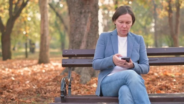 Woman typing text message on mobile phone on park bench