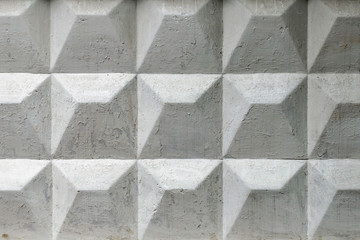 Part of a light concrete fence with rhombuses. White relief concrete wall with geometric shapes.