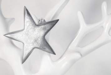 Single star on soft white background. Close up. The sterling silver star hangs on a porcelain tree or antler.