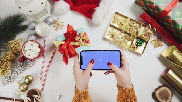 Woman using smartphone with Chroma key, tapping, swipe, scrolling up. Christmas holiday decoration on white table background.