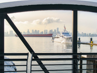 Scenic winter waterfront panorama of city skyline at sunset. A yacht is docked at the pier. Snowy metal fence in the foreground with view to Downtown Vancouver, BC, Canada
