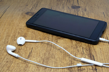 White ear buds headphone with black mobile on wooden brown background - Listening music technology concept