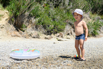 cute little three year old boy in sun hat playing on the sea pebble beach