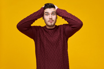 Holiday shopping, November, gifts, Thanksgiving and Christmas concept. Studio shot of surprised bug eyed male in warm sweater holding hands on his head, excited that Black Friday sale is coming