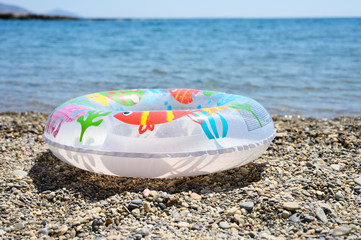 inflatable swimming children circle lies on the pebble beach on the background of water and the sea horizon