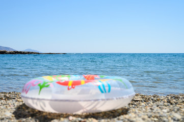 Obraz premium inflatable swimming children circle lies on the pebble beach on the background of water and the sea horizon