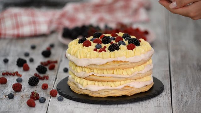 Confectioner girl puts summer berries on a creamy layer cake. Woman preparing a cake with cream and berries.