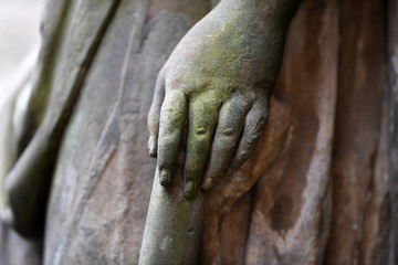The left, moss covered hand of an old sandstone sculpture. 