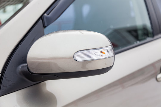 Close-up of the side left mirror with turn signal repeater and window of the car body beige SUV on the street parking after washing and detailing in auto service industry. Road safety while driving