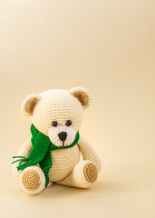Crocheted toy bear in a green scarf on a light background