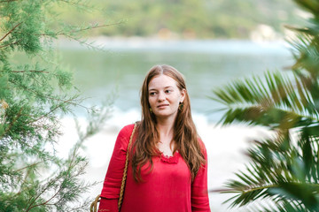 Portrait of beautiful girl with wet hair in a red summer dress on the beach after swimming. Sea nature in soft shades. Full relaxation for body and soul