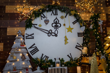 Big decorative clock on the wall with shiny stars, garland lights, wooden toys and candles. Merry Christmas or Happy New Year eve concept. Winter holidays. 