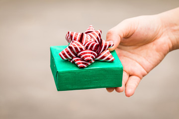 Woman hand hold a green gift box tied with red ribbon for give in the public park, present for...