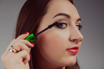 Beauty model teenage girl looking in the mirror and applying mascara make up. Beautiful young woman apply makeup