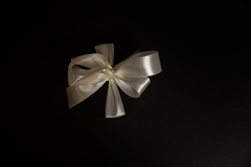 Round black gift box with a white bow on a black background. Card. Space for text. Background.