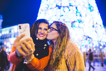 Two girls are taking a picture next to the Christmas lights. They are enjoying together in the city...