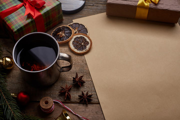 A wish list. Old paper sheet with pencil at grunge wooden background with copy space. Christmas tree, gift, cones, dried citrus fruits, magnifying glass, cinnamon, scissors. Cup of tea.