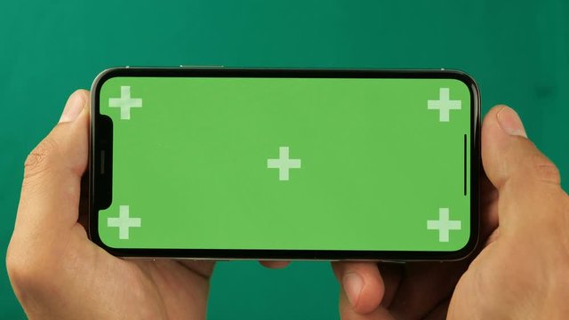 Close up man holds a smartphone with green screen chroma key in his hands in a horizontal position and flips through photos. Good footage for the slideshow