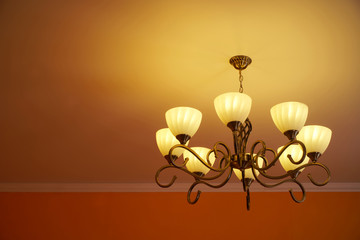 Wrought iron vintage retro chandelier with eight incandescent lamps. Warm yellow light. Homeliness.