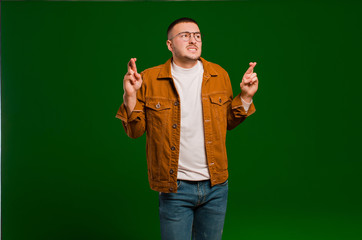 young handsome man crossing fingers anxiously and hoping for good luck with a worried look against...