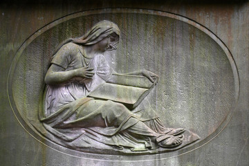 An old, weathered sandstone relief of a woman who reads a book. A tombstone on a 400 years old...